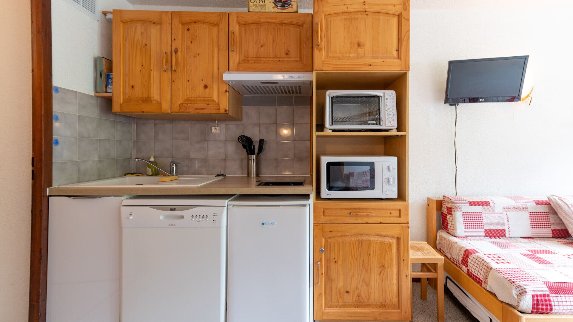 A compact kitchen with wooden cabinets, a dishwasher, two microwaves, and a small table.
