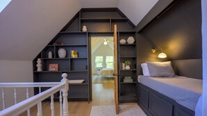 Quarto em estilo loft com cama embutida, um cantinho de leitura com estantes e uma escada.