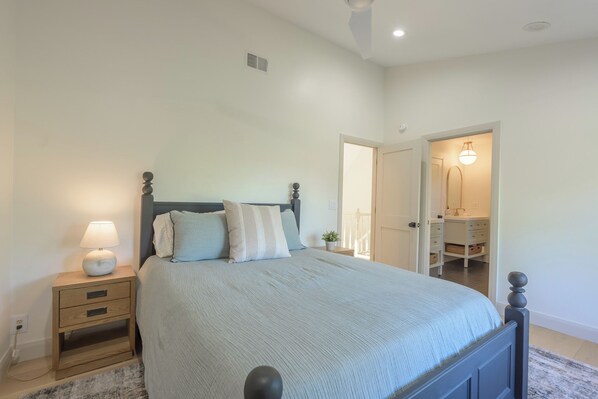 A bedroom with a bed, bedside table, lamp, and a door leading to a bathroom.