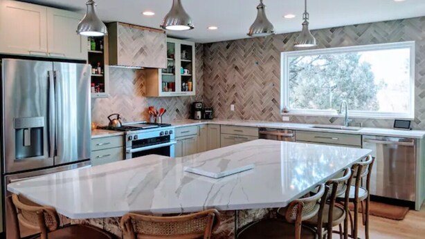 A modern kitchen with a large island, stainless steel appliances, and pendant lighting.