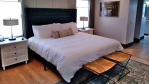 A modern hotel room with a large bed, bedside tables, a small table, and a painting on the wall.