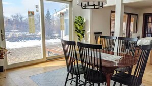 A dining area with a large table and chairs, a potted plant, and a view through a glass door.