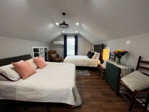 A bedroom with two beds, a chair, a desk, and a window.