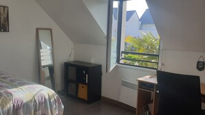 Une chambre à coucher comprenant un lit, un bureau, une commode, un miroir et une fenêtre donnant sur un paysage verdoyant.