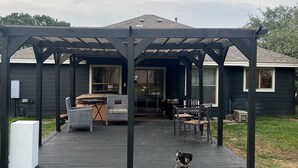 A covered outdoor deck with a pergola, a dining area with chairs and a table, and a dog standing on the deck. - Lake Time at Beautiful Buchanan (Burnet)