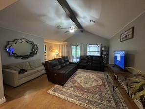 Un salon doté d’un ventilateur de plafond, d’un grand miroir, d’un canapé, d’une causeuse, d’un tapis et d’un téléviseur.
