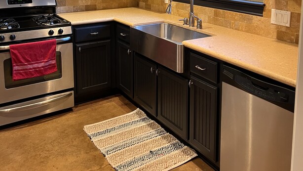 A modern kitchen with dark cabinetry, stainless steel appliances, a large window, and a decorative backsplash. - Lake Time at Beautiful Buchanan (Burnet)