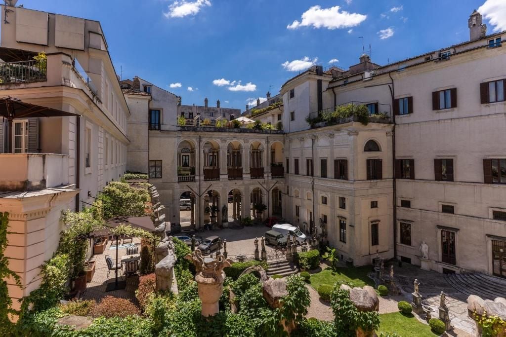 A courtyard with a central open space surrounded by buildings with arched doorways and a statue in the middle.
