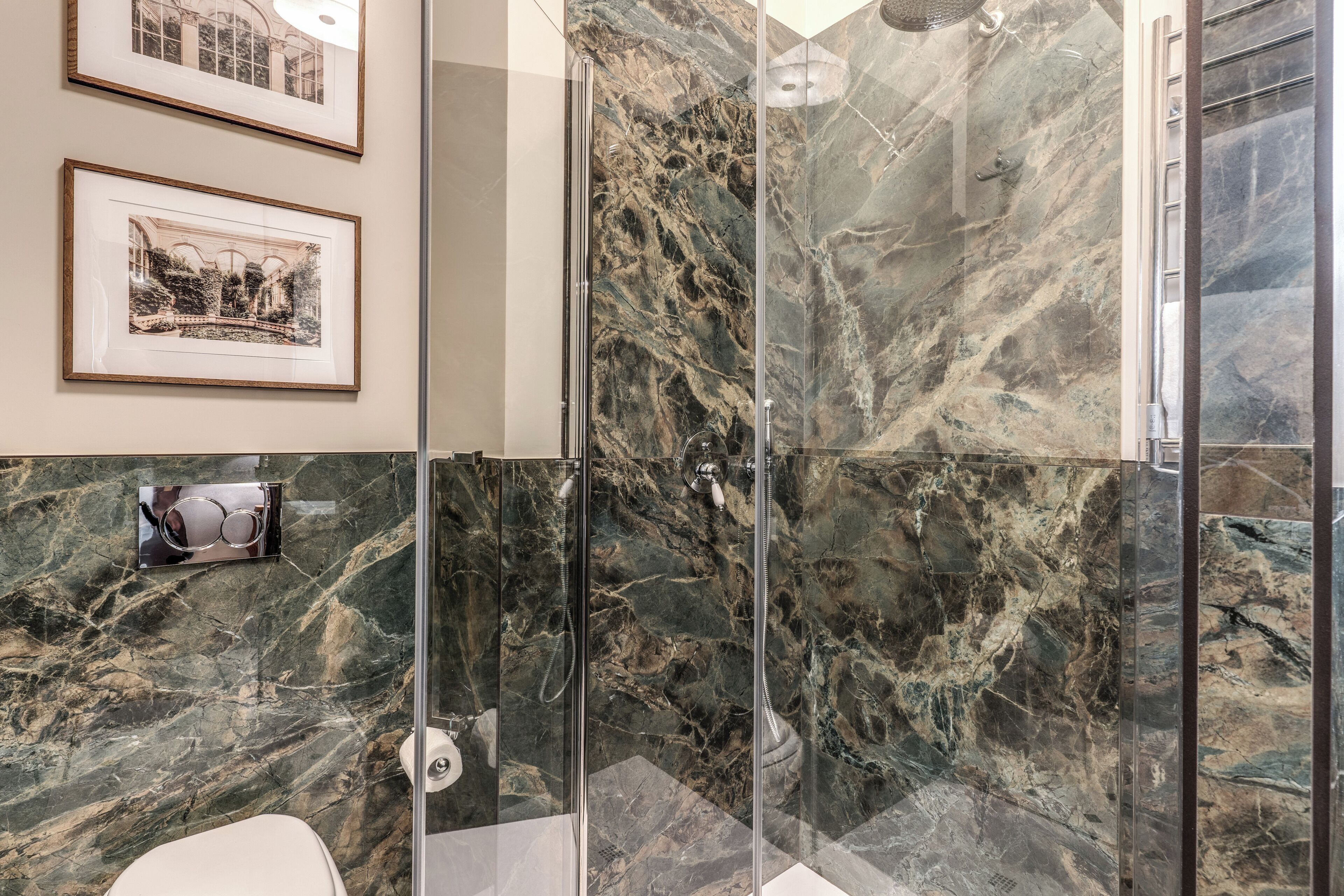 A bathroom with a glass shower enclosure, marble walls, and framed pictures on the wall.