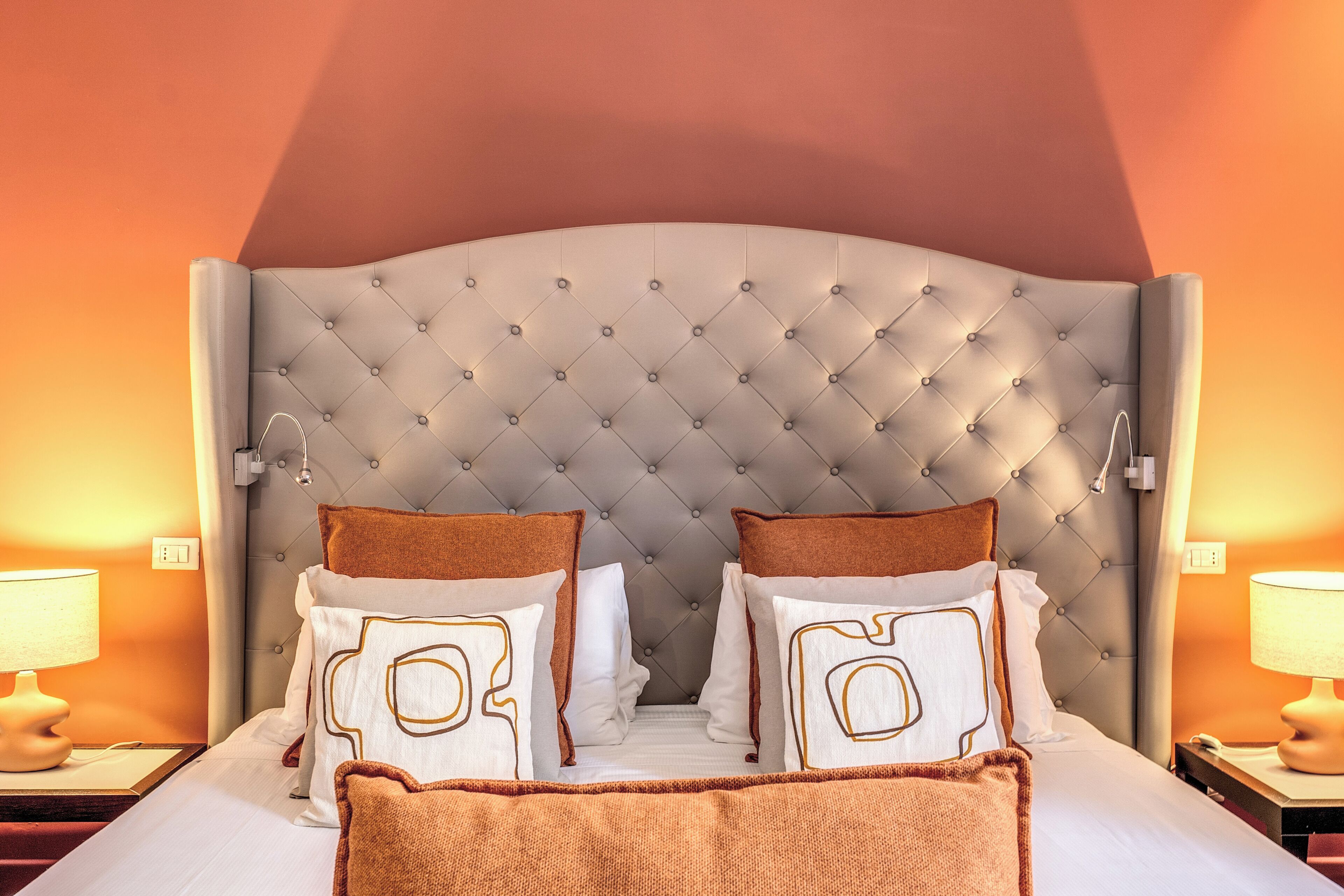 A neatly made bed with a tufted headboard, two pillows with a geometric design, and a brown throw blanket.