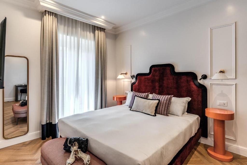 Una habitación de hotel con una cama grande, dos mesitas de noche, un espejo y una ventana con cortinas.