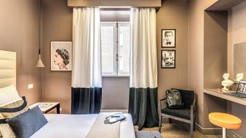 Une chambre d’hôtel avec un lit, un bureau et une chaise, une fenêtre avec des rideaux et des œuvres d’art accrochées aux murs.