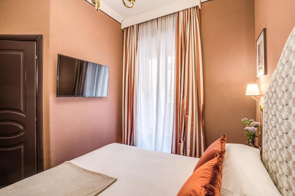 A hotel room with a bed, a television, curtains, a door, and a lamp.