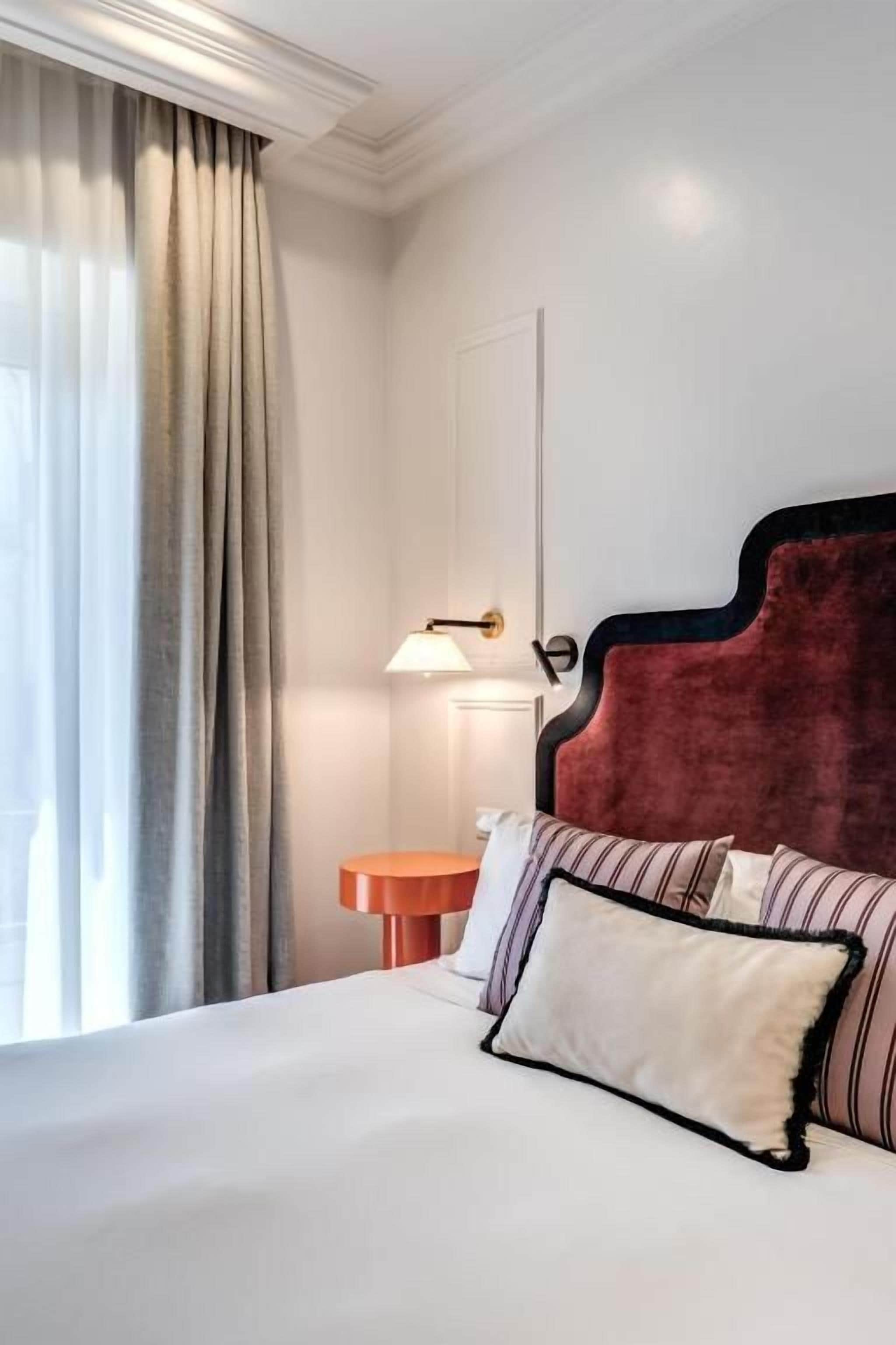 A hotel room with a large bed, a round side table, a lamp, and a view of the outdoors.