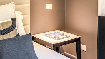 Un dormitorio moderno con cama, mesita de noche con un libro, lámpara de pared y una obra de arte enmarcada.