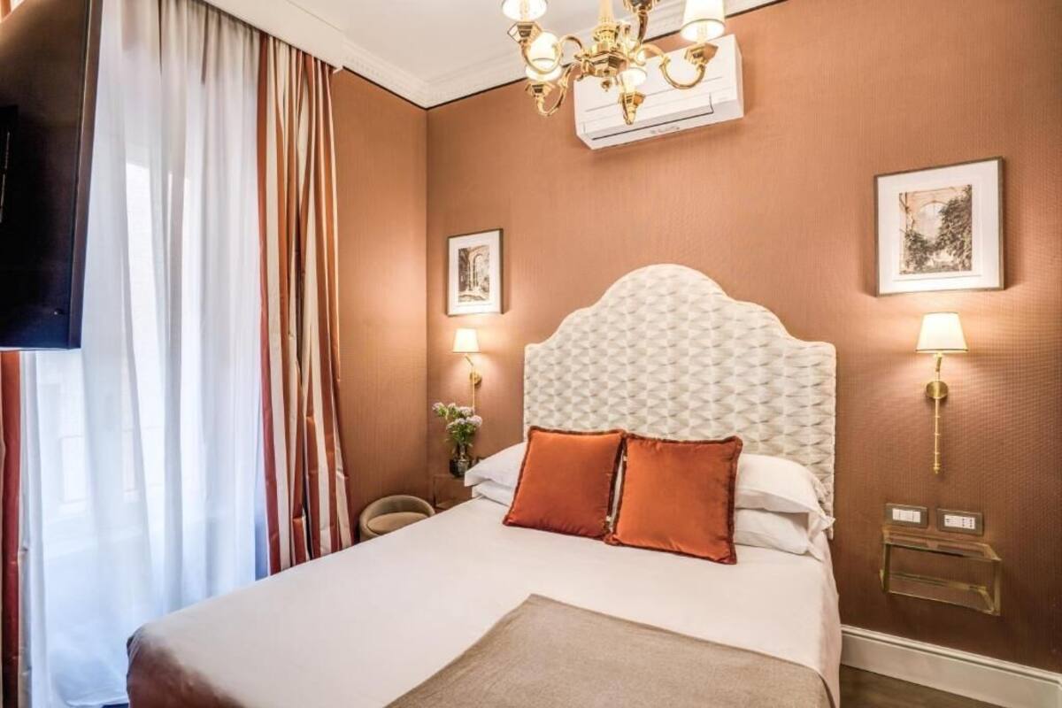 Habitación de hotel con una cama grande, un candelabro, un televisor de pantalla plana y un aire acondicionado instalado en la pared.