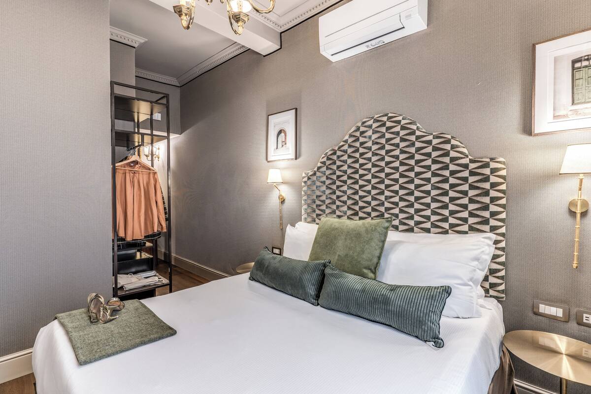 Una habitación de hotel con cama, armario, mesita de noche, lámpara y aire acondicionado.