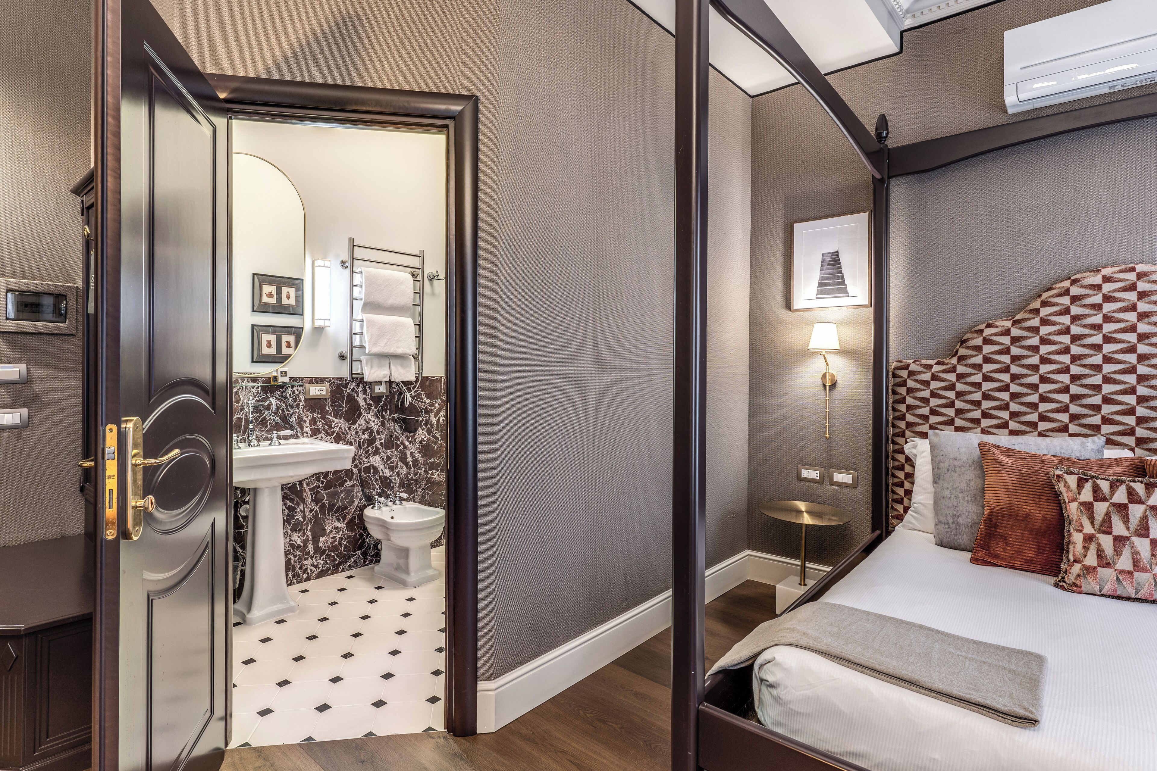 A hotel room with a bed, a bedside table, a lamp, a mirror, a sink, and a toilet.