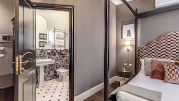 A hotel room with a bed, a bedside table, a lamp, a mirror, a sink, and a toilet.