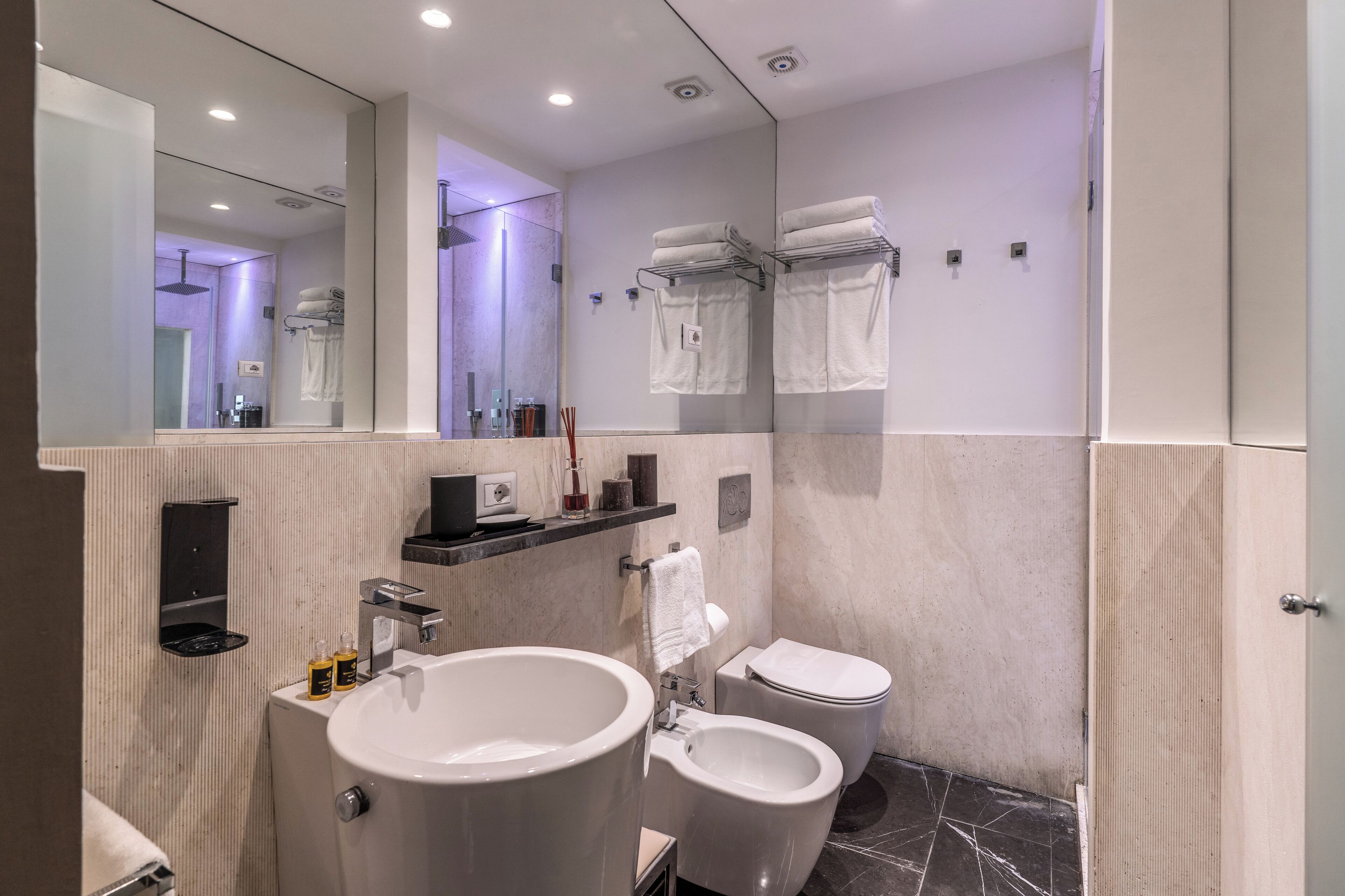 Un baño moderno con un espejo grande, un lavabo, un bidé y un inodoro.
