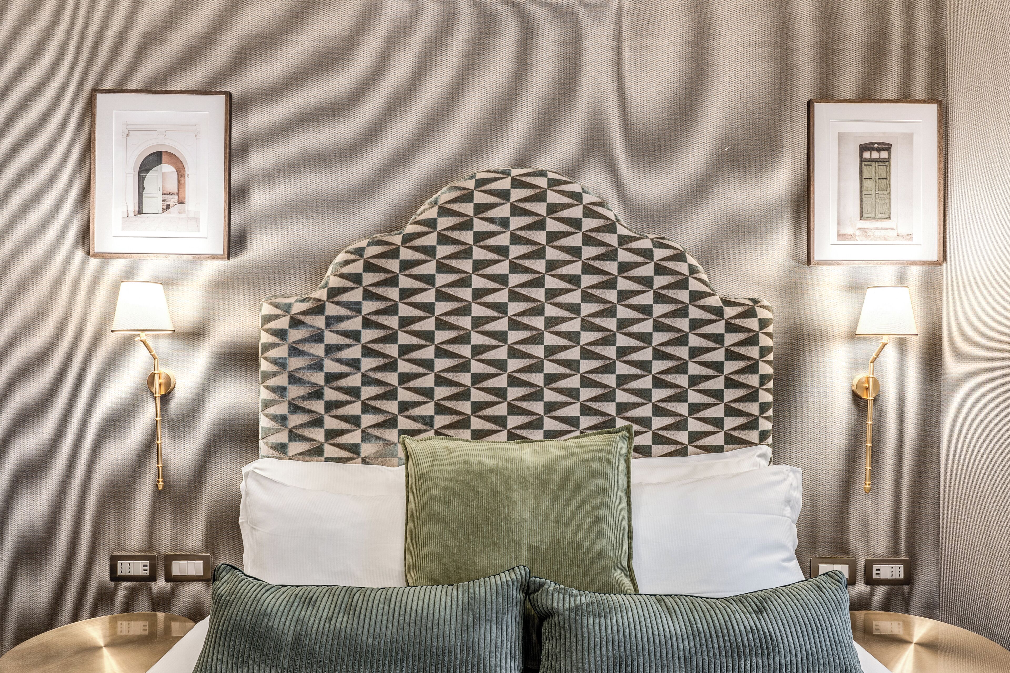 Habitación de hotel con cabecera de diseño geométrico, dos lámparas de noche y cuadros en las paredes.