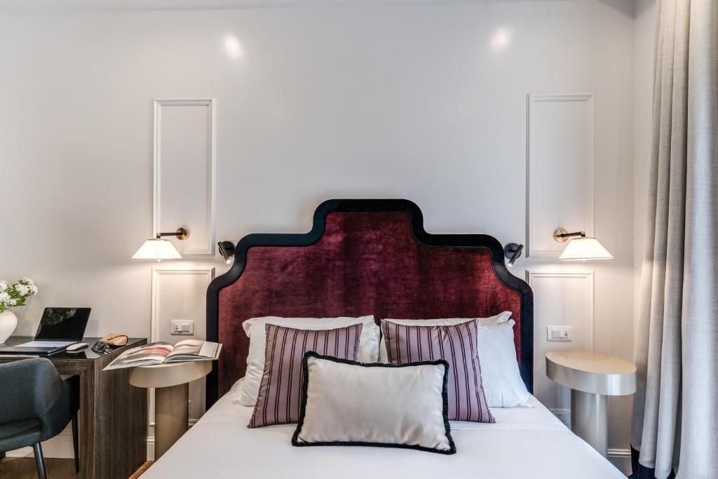 A hotel room with a large bed, two bedside tables, a desk with a chair, and a lamp.