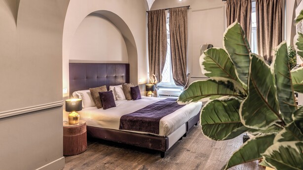 A bedroom with a large bed, a nightstand, a lamp, and a window with curtains.