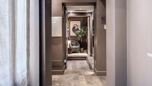 A narrow hallway with a modern design, featuring a chair and a potted plant in the center.