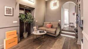 A modern living room with a sofa, a coffee table, and a plant. There are two Louis Vuitton boxes on the floor.