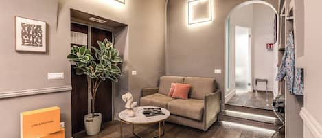 A modern living room with a sofa, a coffee table, and a plant. There are two Louis Vuitton boxes on the floor.