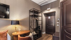 A hotel room with a bed, a desk with a lamp, a chair, a wardrobe, and a door.