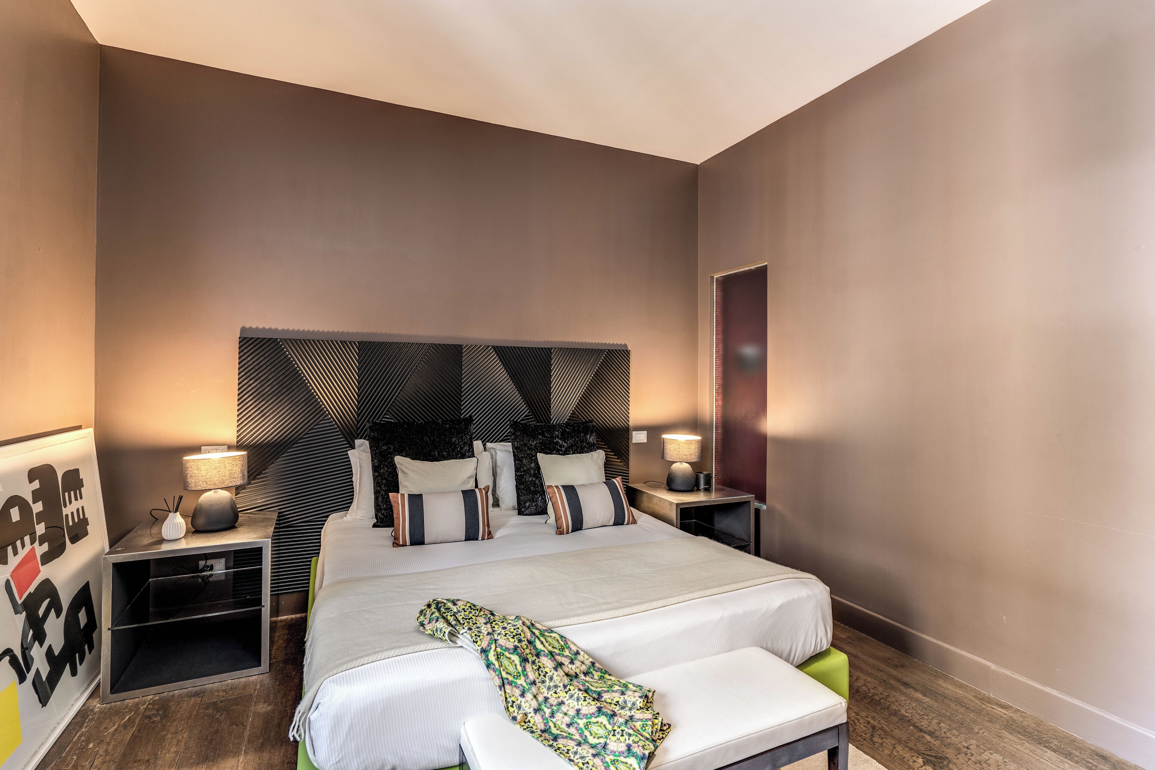 A modern hotel room with a large bed, bedside tables, and a headboard with a geometric pattern.