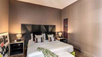 A modern hotel room with a large bed, bedside tables, and a headboard with a geometric pattern.