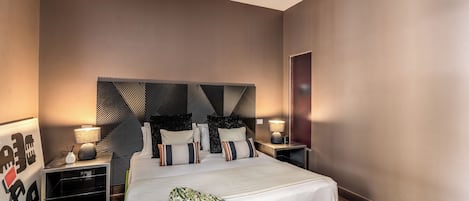 Une chambre d’hôtel moderne avec un grand lit, des tables de chevet et une tête de lit ornée d’un motif géométrique.
