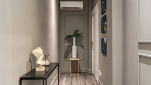 A hallway with a marble floor, a black console table with a bust sculpture, a white vase with a plant, and a wall-mounted air conditioner.