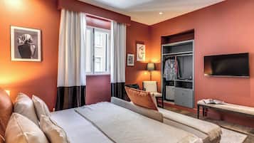 Une chambre d’hôtel avec un lit, une banquette, une télévision, une armoire et une fenêtre avec des rideaux.