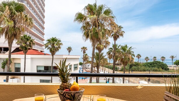 A balcony with a table set for breakfast, overlooking a beach with palm trees and a hotel in the background. - Charming apartment near beach, sea view  REF038 (Torremolinos)