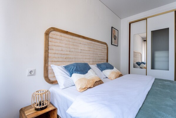 Een netjes opgemaakt bed met een houten hoofdbord, een nachtkastje met een decoratieve lamp, en een spiegel aan de muur.