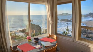 Un comedor con una mesa dispuesta para dos personas, con vistas a la costa, terreno rocoso y el mar.
