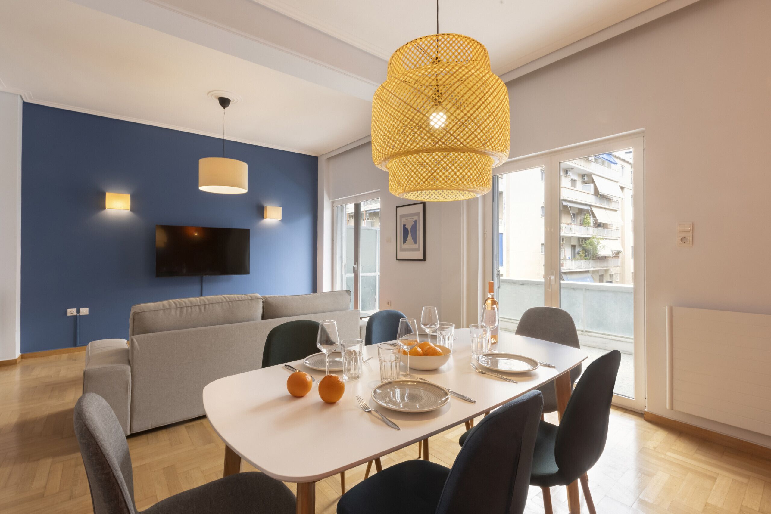 A modern living room with a sofa, dining table, chairs, a TV, and a large window with a view.