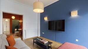 A living room with a sofa, a coffee table, and a TV mounted on the wall. - Volanaki4 - A happy 2 Bdr apartment that has a (Athens)