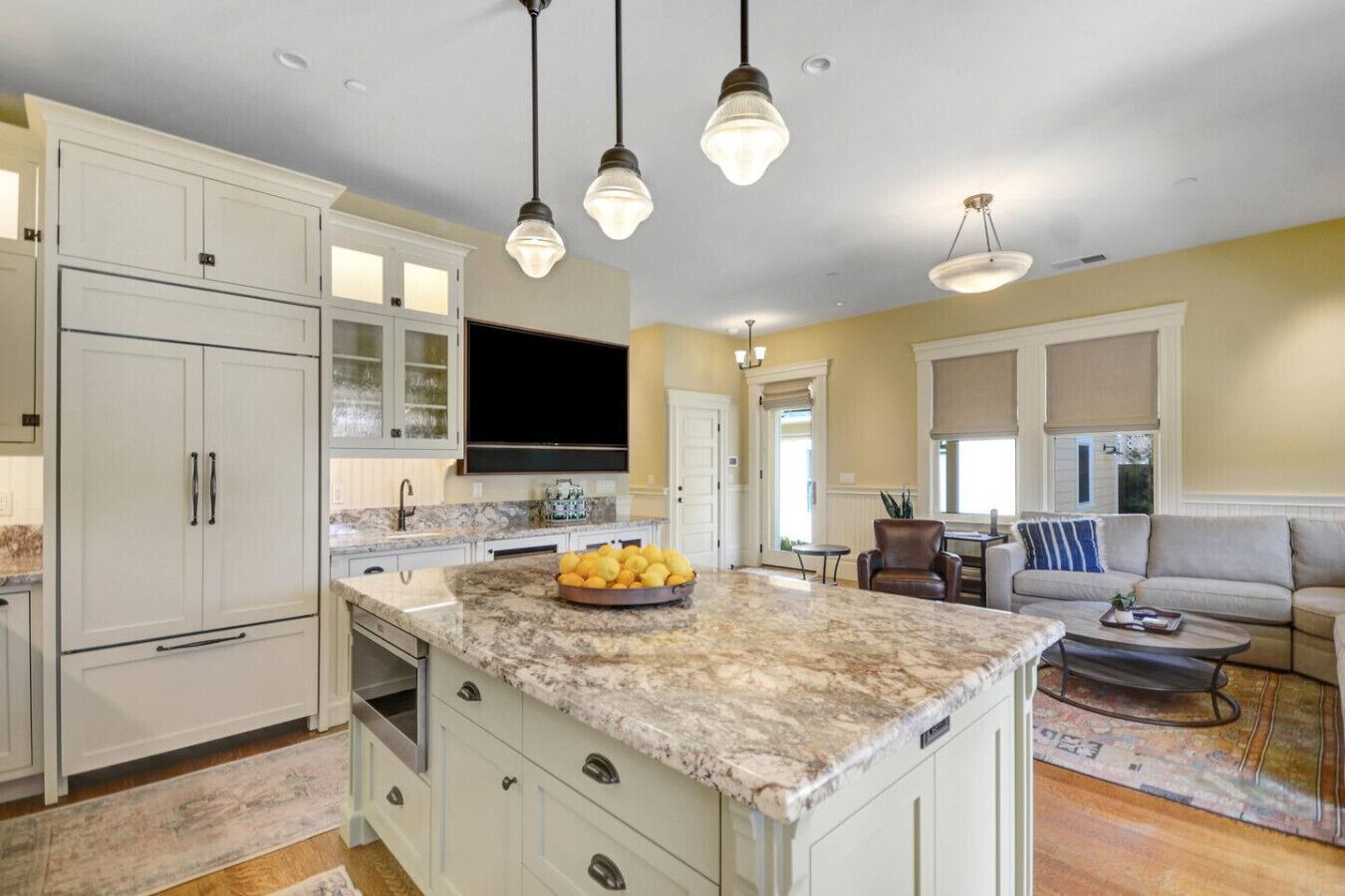 A spacious kitchen with a large island, white cabinetry, and a flat-screen TV.