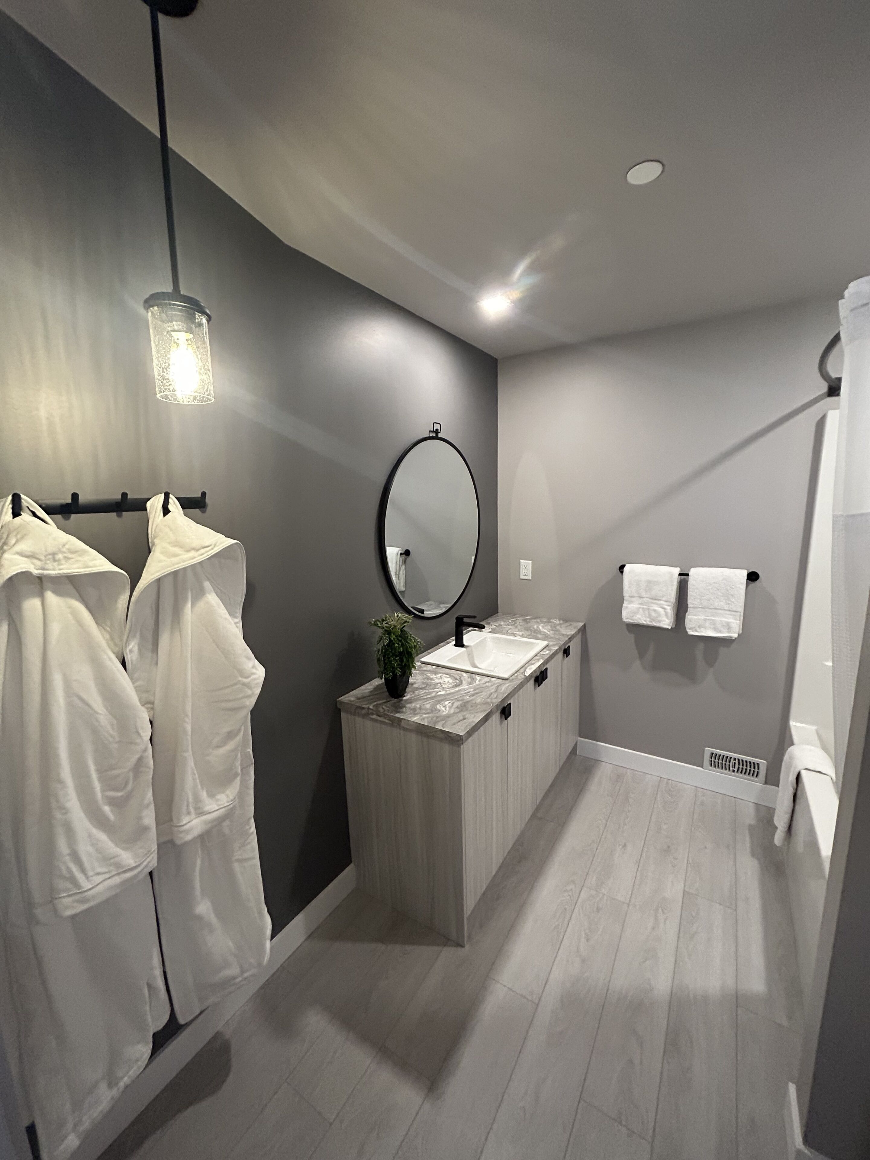 Ein modernes Badezimmer mit einem Holzkosmetikschrank, einem großen Spiegel und einer Pendelleuchte.