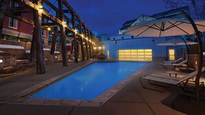 A swimming pool with lounge chairs and umbrellas, surrounded by stone walls and wooden beams.