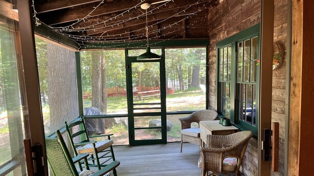 A wooden porch with wicker furniture and a view of the forest.
