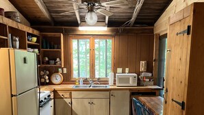 A rustic kitchen with wooden cabinets, a vintage refrigerator, a microwave, and a wooden dining table with chairs.