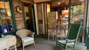 A cozy room with a wooden floor, a wicker chair, a wooden table, and a green chair.