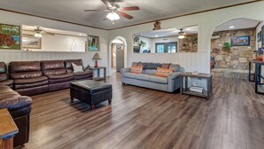 A spacious living room with a brown leather sofa, a blue sofa with 'welcome' pillows, a coffee table, and a stone accent wall. - Secluded Upscale Smoky Mountain Retreat - Hot Tub, Game Room,  Near Pigeon Forge (Sevier County)