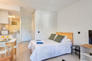 Une chambre avec un lit, une table de chevet et un téléviseur. Il y a également une petite cuisine équipée d’un four à micro-ondes et d’une machine à café.