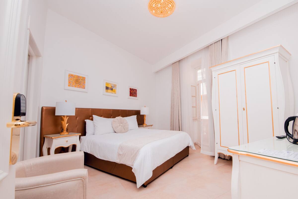A hotel room with a large bed, a desk, a wardrobe, and artwork on the walls.